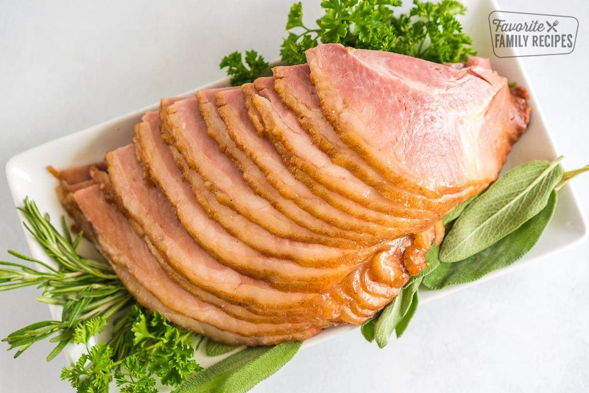 Crock Pot Ham fanned out on a serving platter with fresh herbs