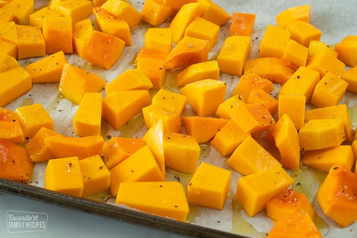Uncooked butternut squash with olive oil, salt, and pepper on a baking sheet