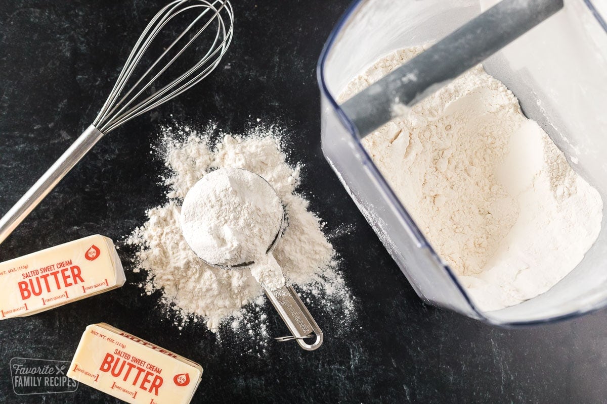 flour, butter, and a whisk on a table top. Ingredients to make a roux.