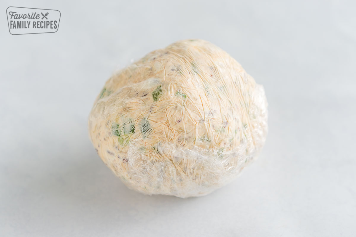 A cheese ball rolled into plastic wrap to set