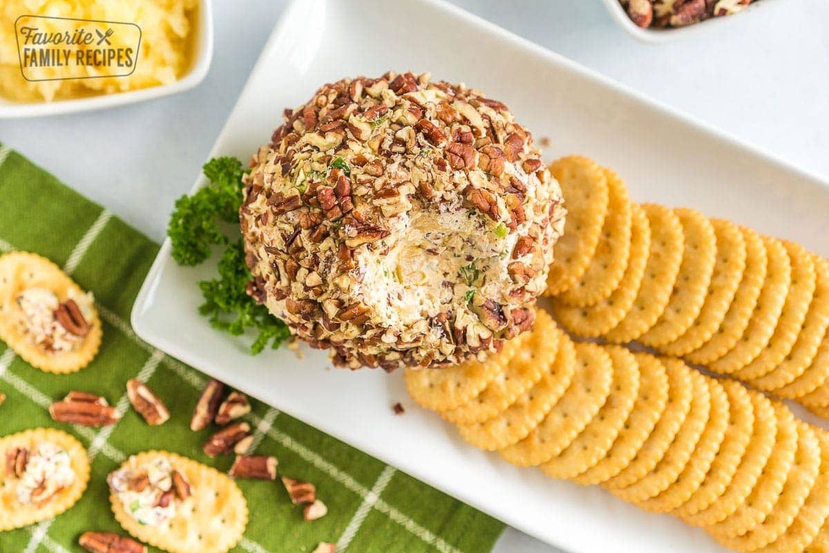 A cheese ball with some scooped out on a platter with crackers.