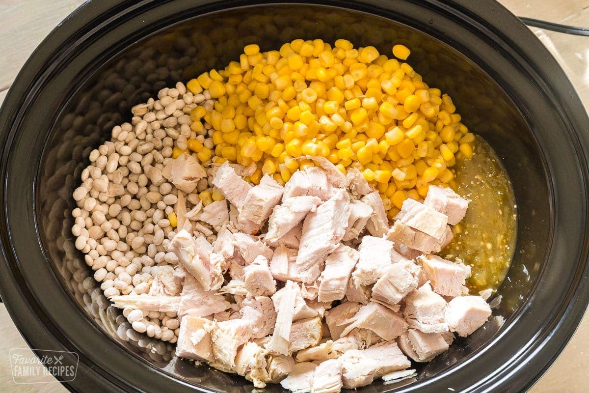 A Crock Pot with white beans, chopped chicken, green salsa, and corn