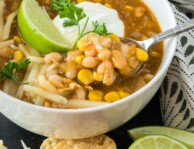 A bowl of white chicken chili garnished with limes and sour cream
