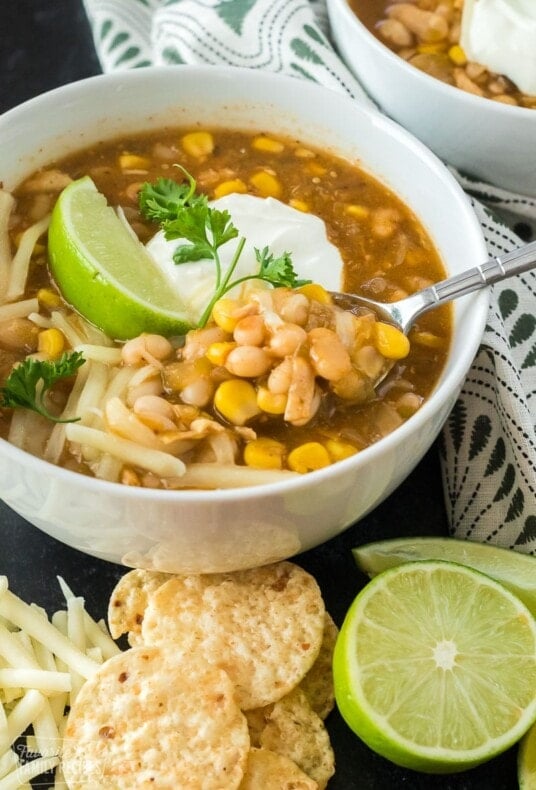 A bowl of white chicken chili garnished with limes and sour cream