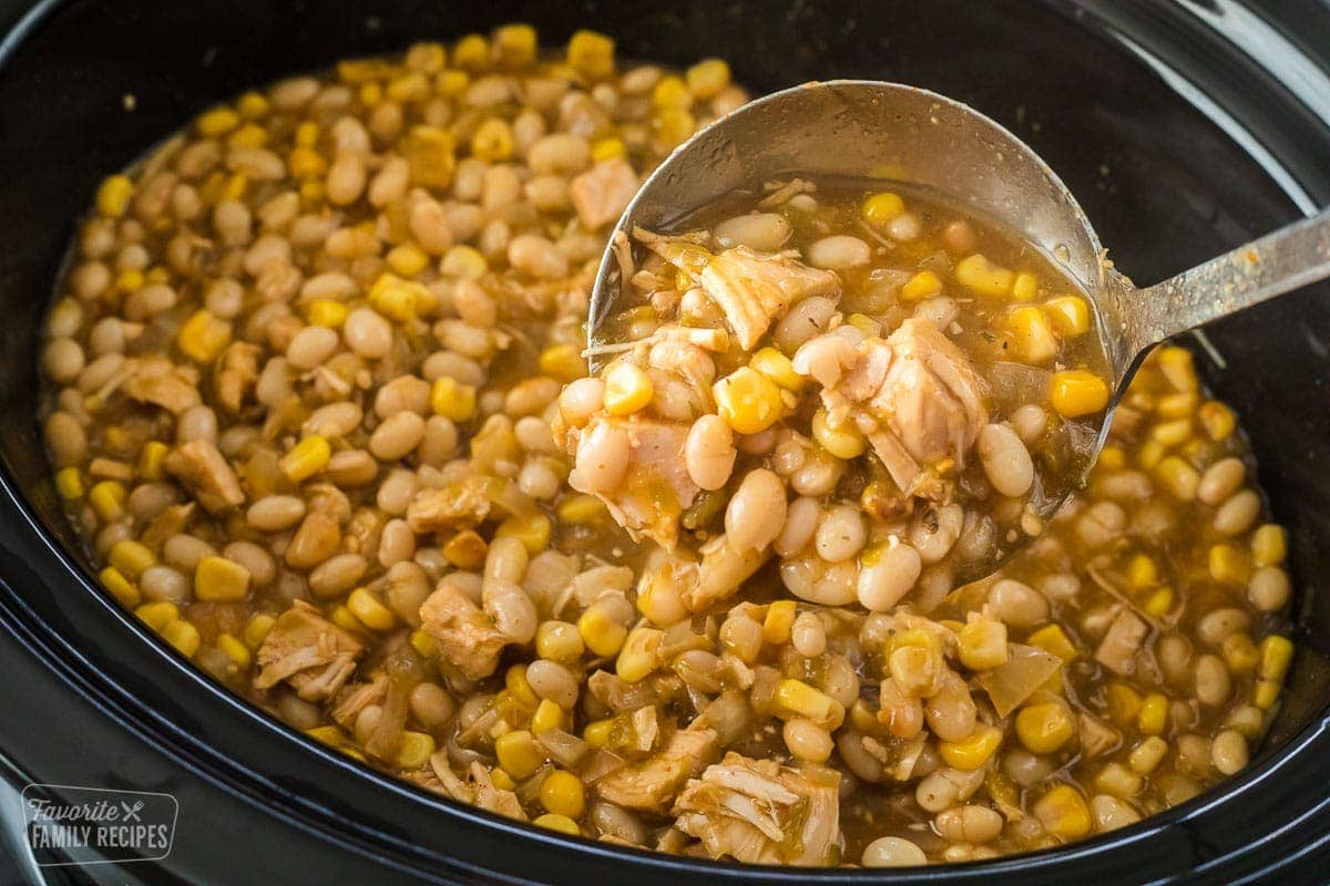 A close up of a Crock Pot with white chicken chili and a scoop being lifted from the pot