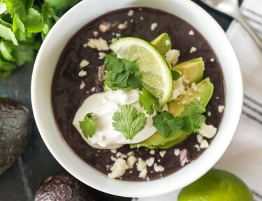 Black bean soup on a table with avocados and a lime