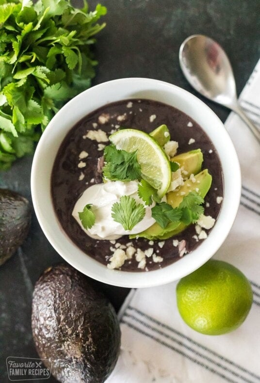 Black bean soup on a table with avocados and a lime