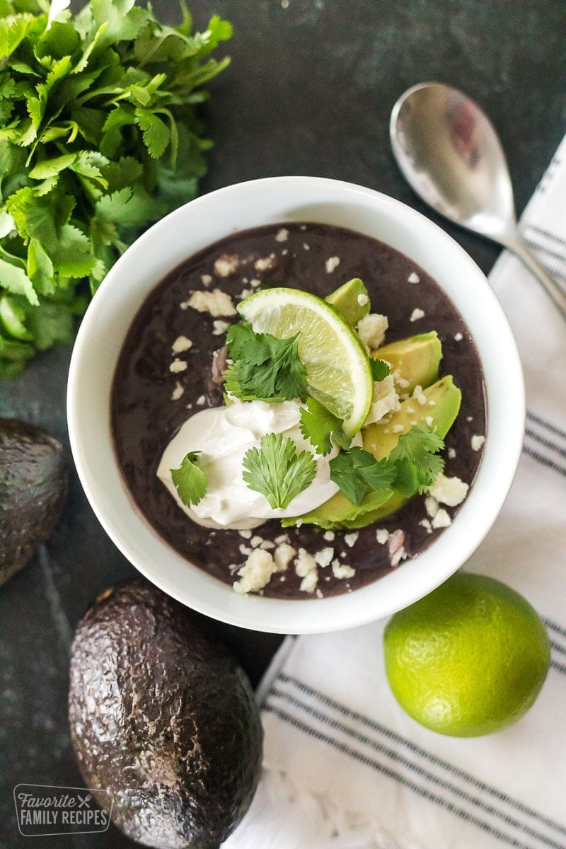 Black bean soup on a table with avocados and a lime