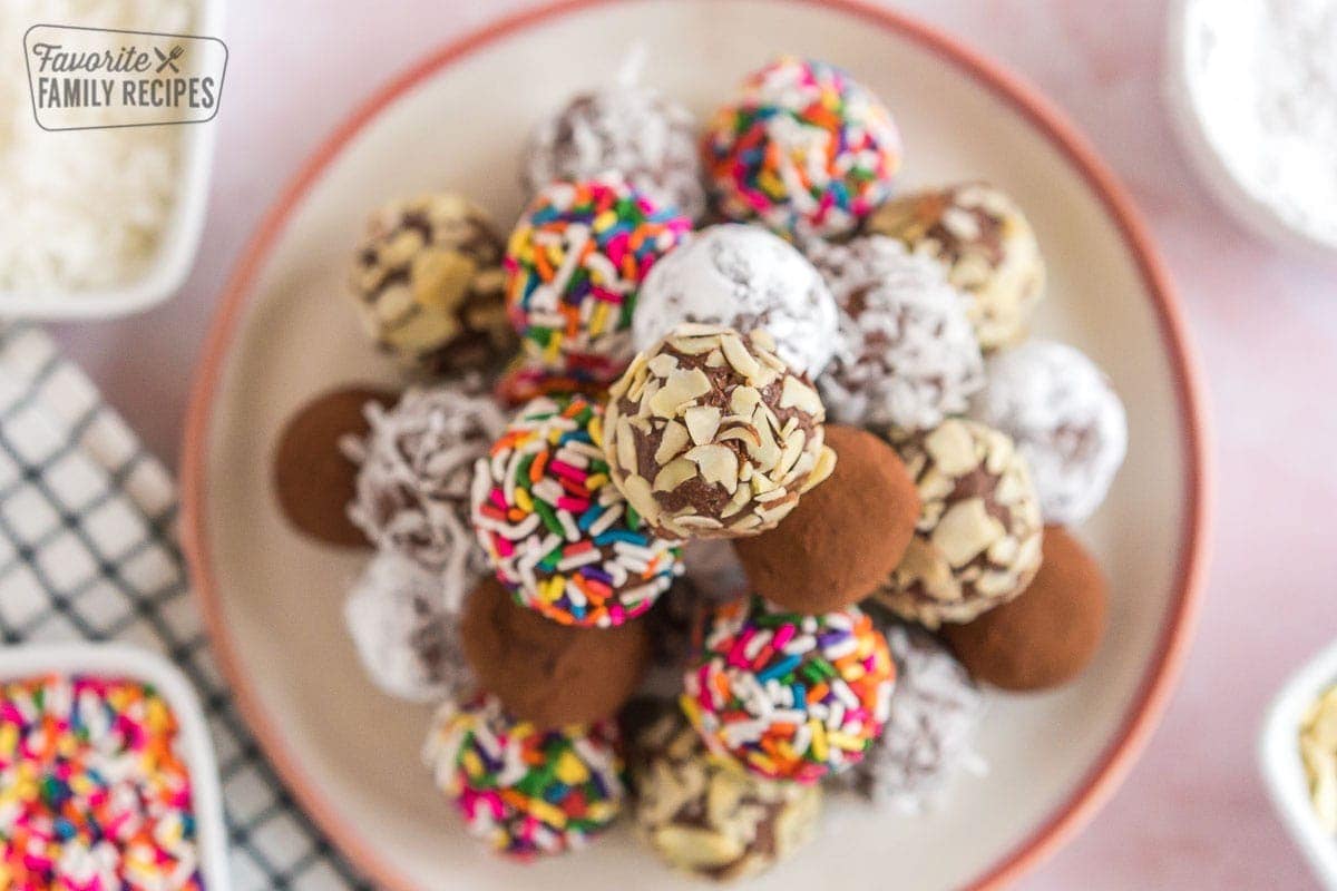 A stack of chocolate truffles on a plate, the top one being rolled in almond pieces.