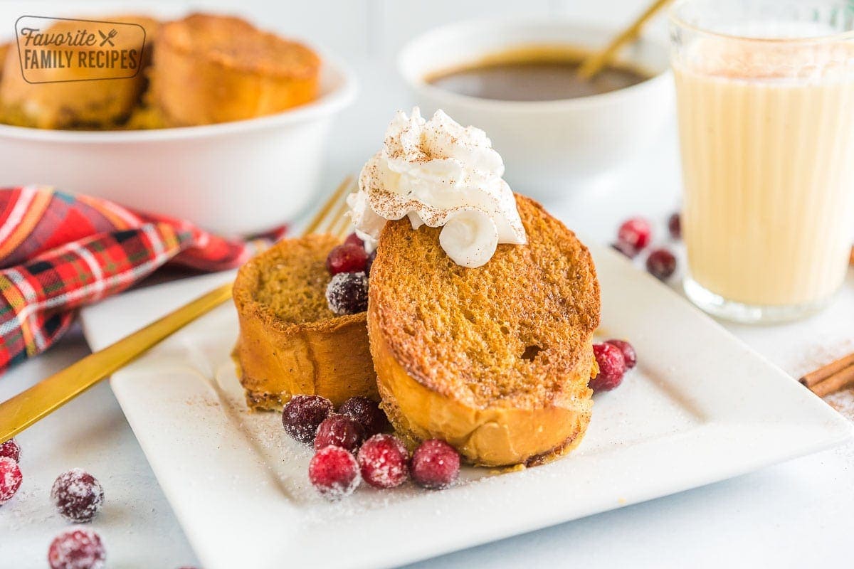 Eggnog French Toast on a plate with sugared cranberries and whipped cream.