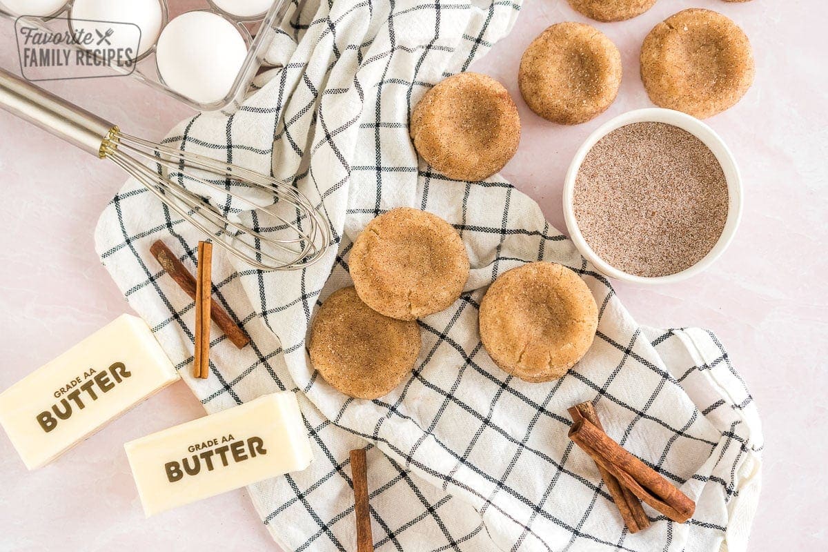 Snickerdoodles on a cloth with cinnamon sugar mixture in a bowl. 