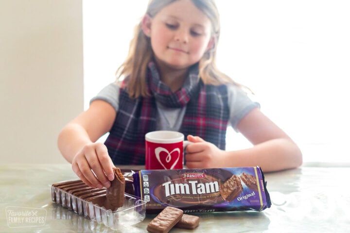 A girl picking up a Tim Tam to do the Tim Tam Slam
