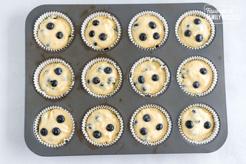 Muffin batter scooped into cupcake liners and topped with blueberries