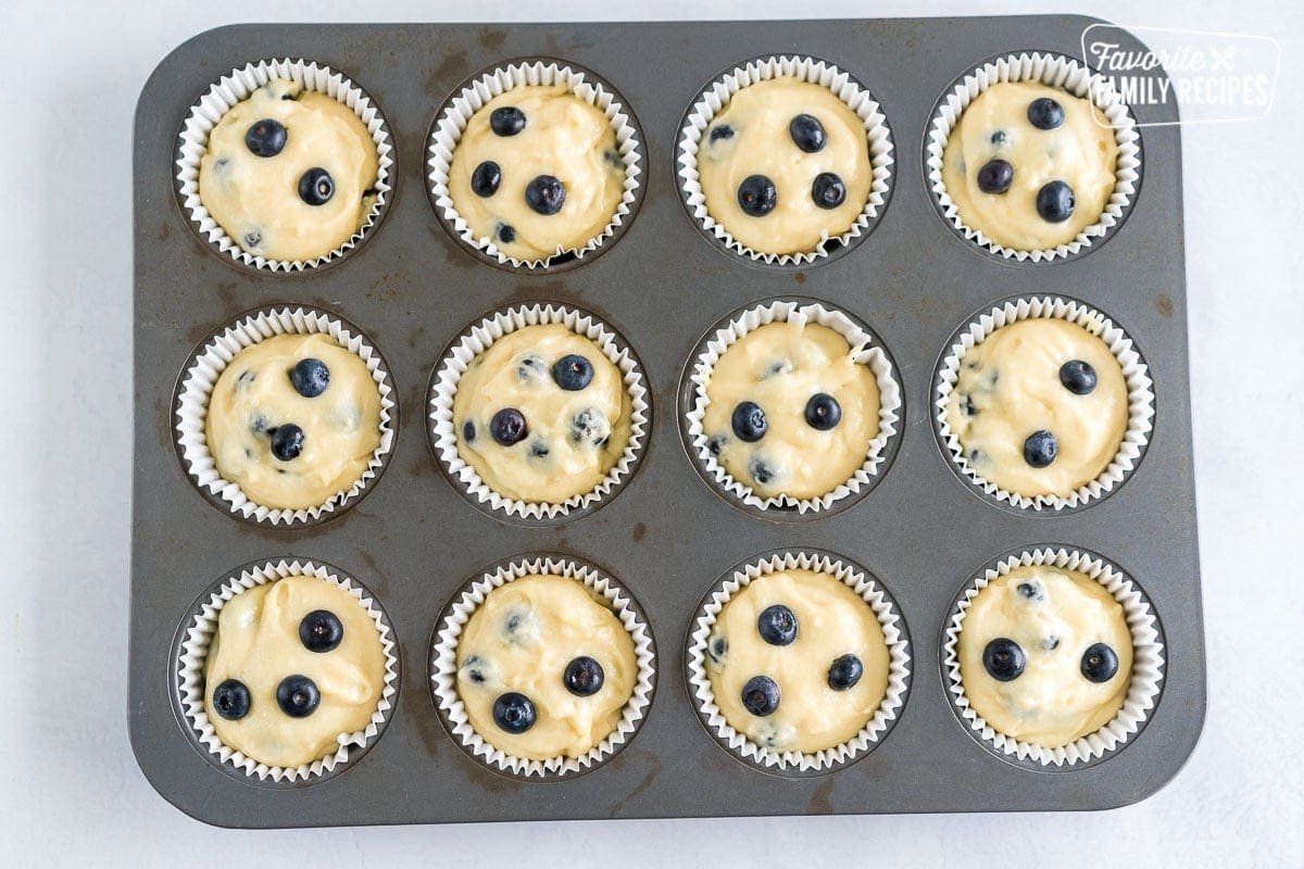 Muffin batter scooped into cupcake liners and topped with blueberries.