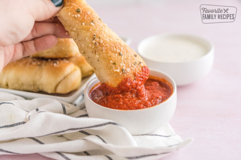 A breadstick being dipped in marinara sauce