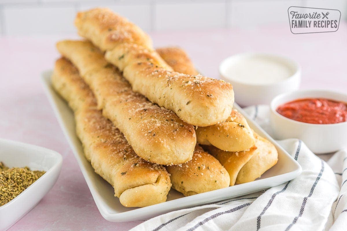 Breadsticks on a platter surrounded by dipping sauce.