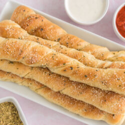 Breadsticks on a platter surrounded by dipping sauce.