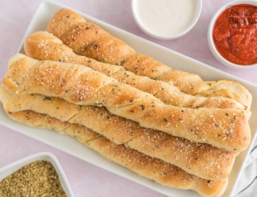 Breadsticks on a platter surrounded by dipping sauce.