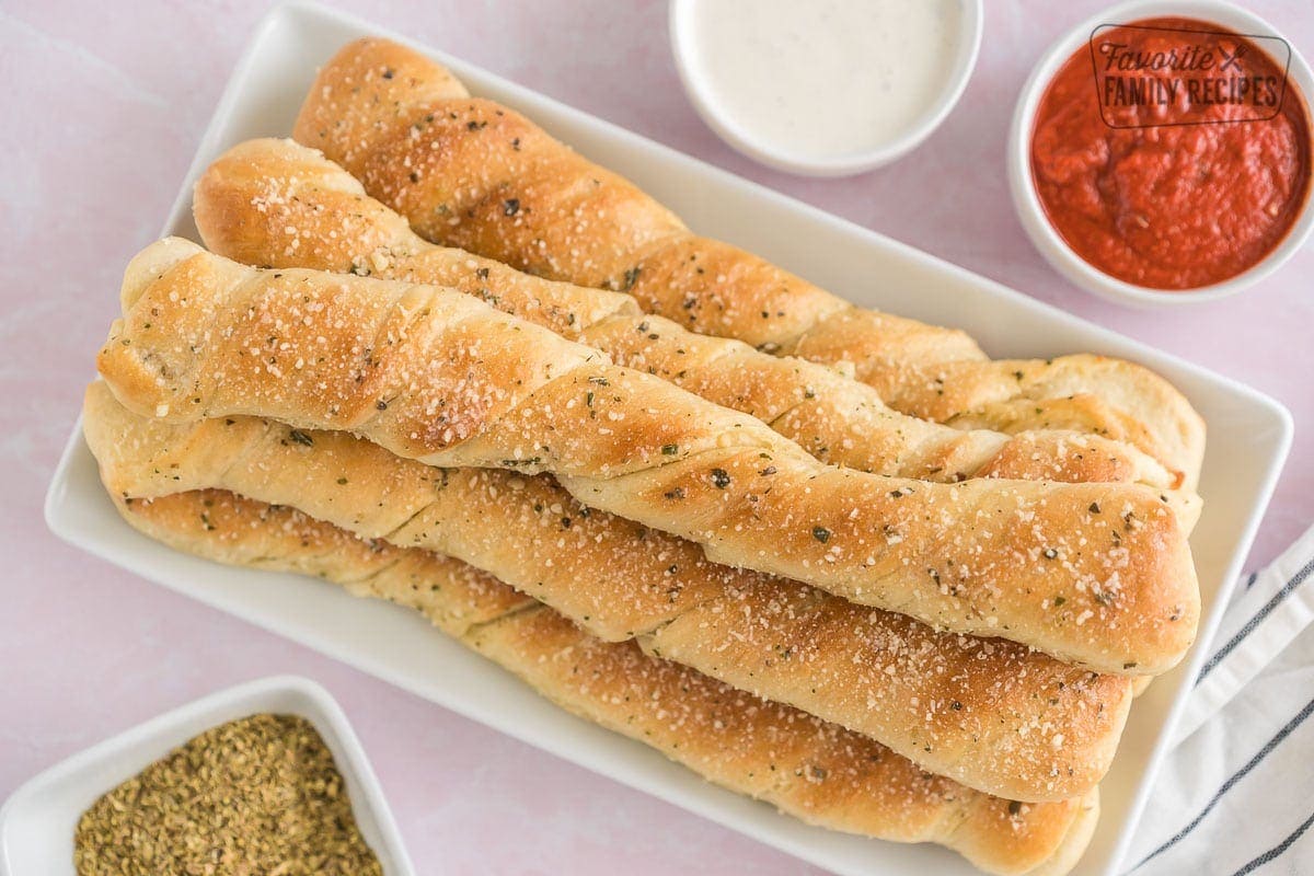 Breadsticks on a platter surrounded by dipping sauce.