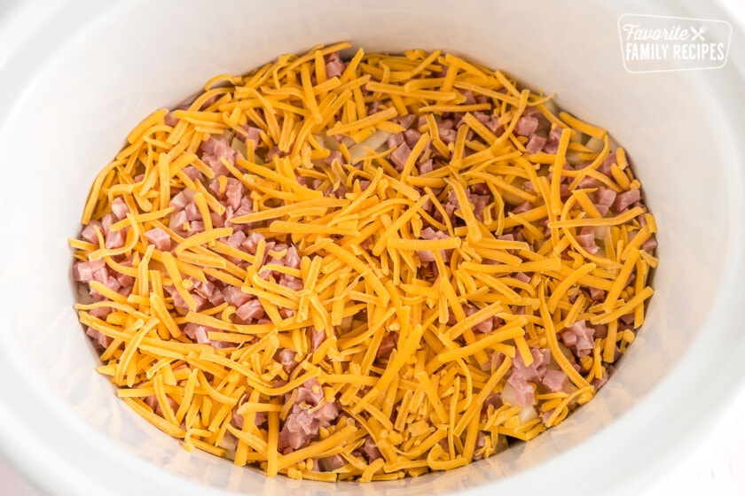 A crock pot filled with potatoes, cheese, and ham