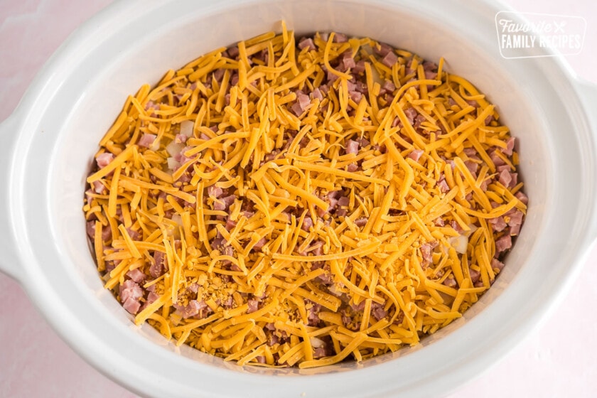 A crock pot filled with potatoes, cheese, and ham