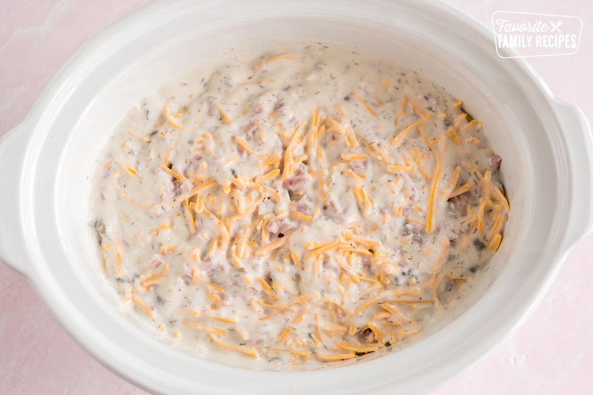 A crock pot full of potatoes, cheese, ham, and cream of mushroom soup