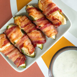 Bacon Wrapped Jalapeños poppers on a plate with ranch for dipping.