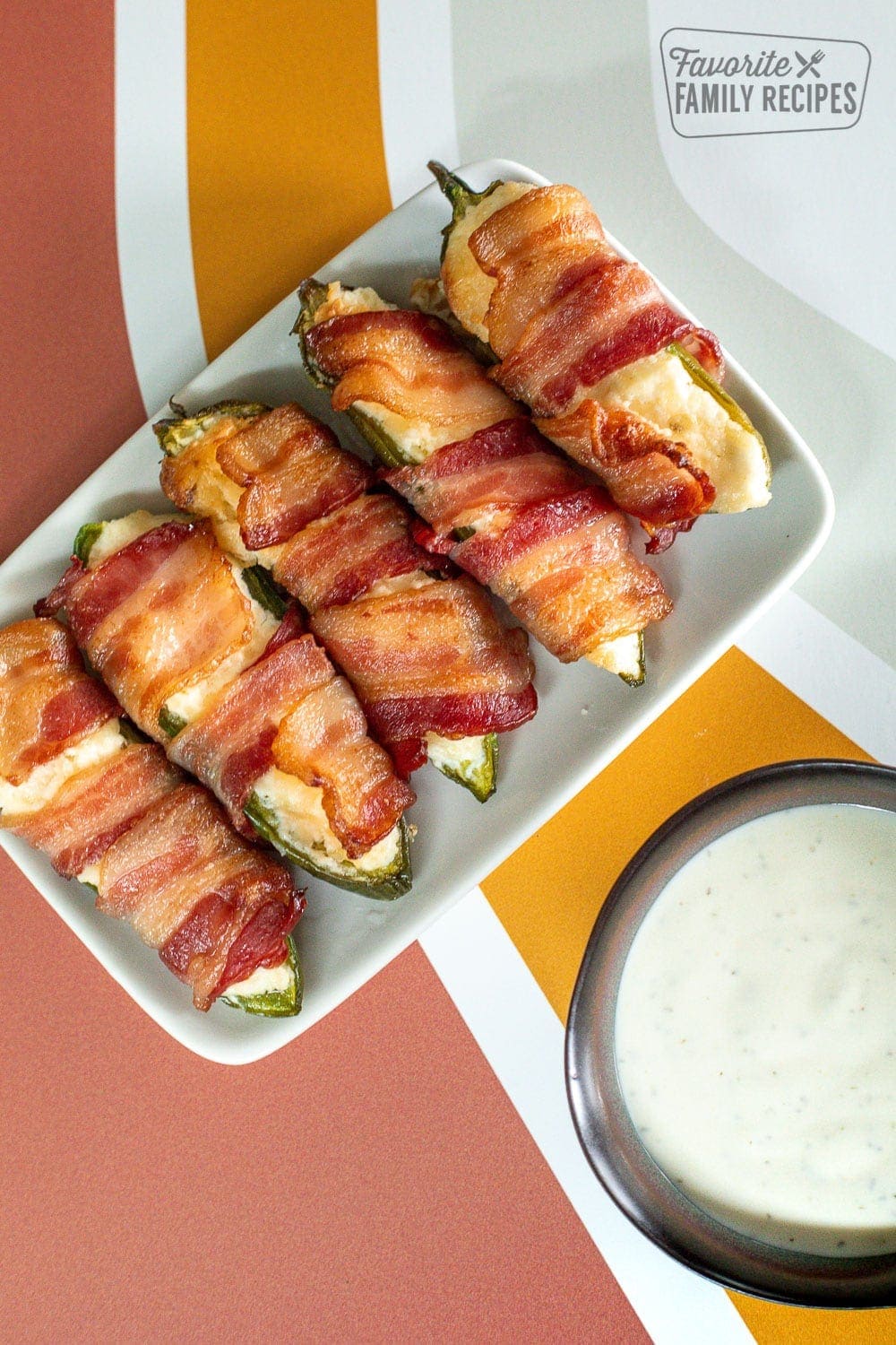 Bacon Wrapped Jalapeños poppers on a plate with ranch for dipping.