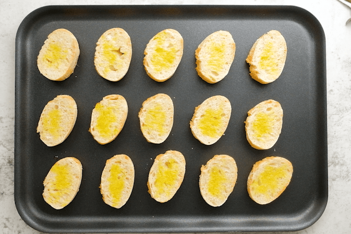 Baguette slices brushed with olive oil on a baking sheet.