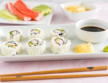 A California roll on a plate with soy sauce, ginger, and wasabi