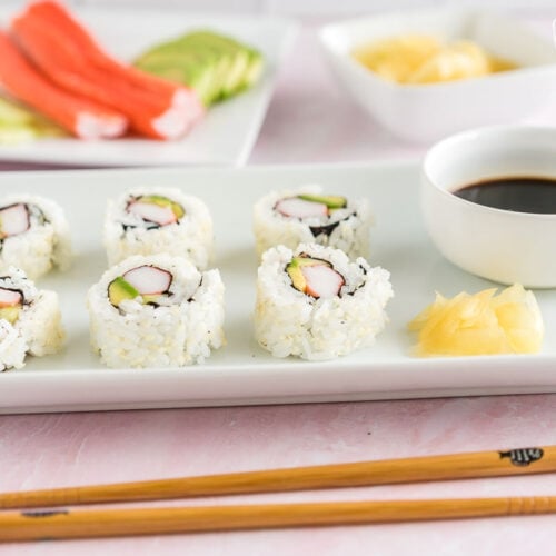 A California roll on a plate with soy sauce, ginger, and wasabi