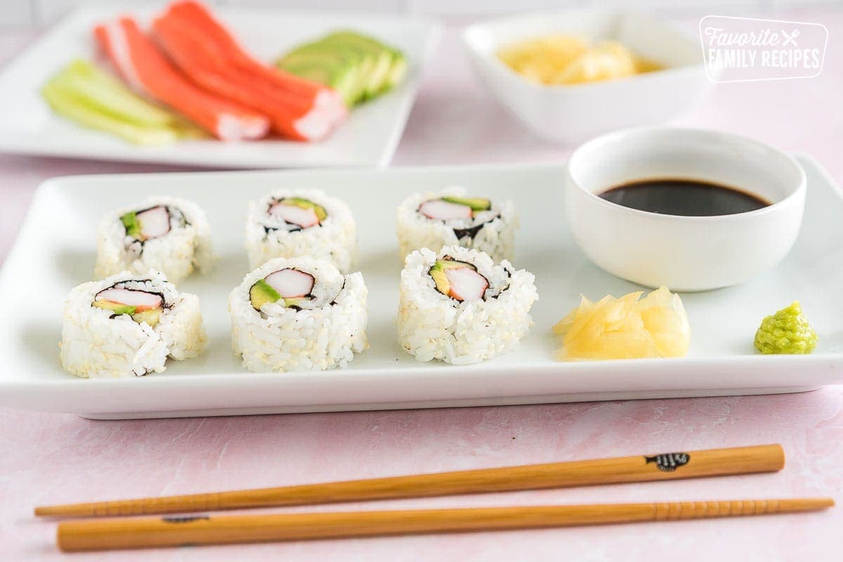 A California roll on a plate with soy sauce, ginger, and wasabi