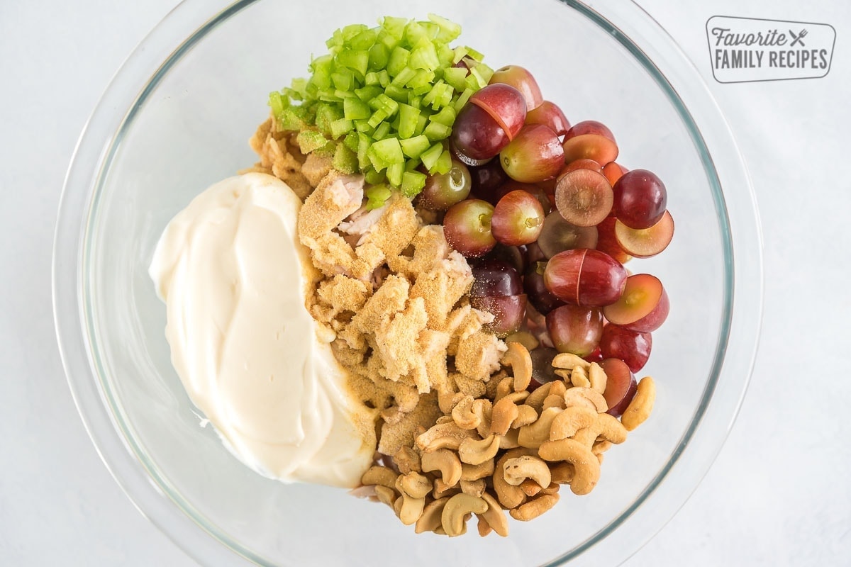 Chicken, grapes, celery, mayonnaise, cashews, and spices in a glass bowl