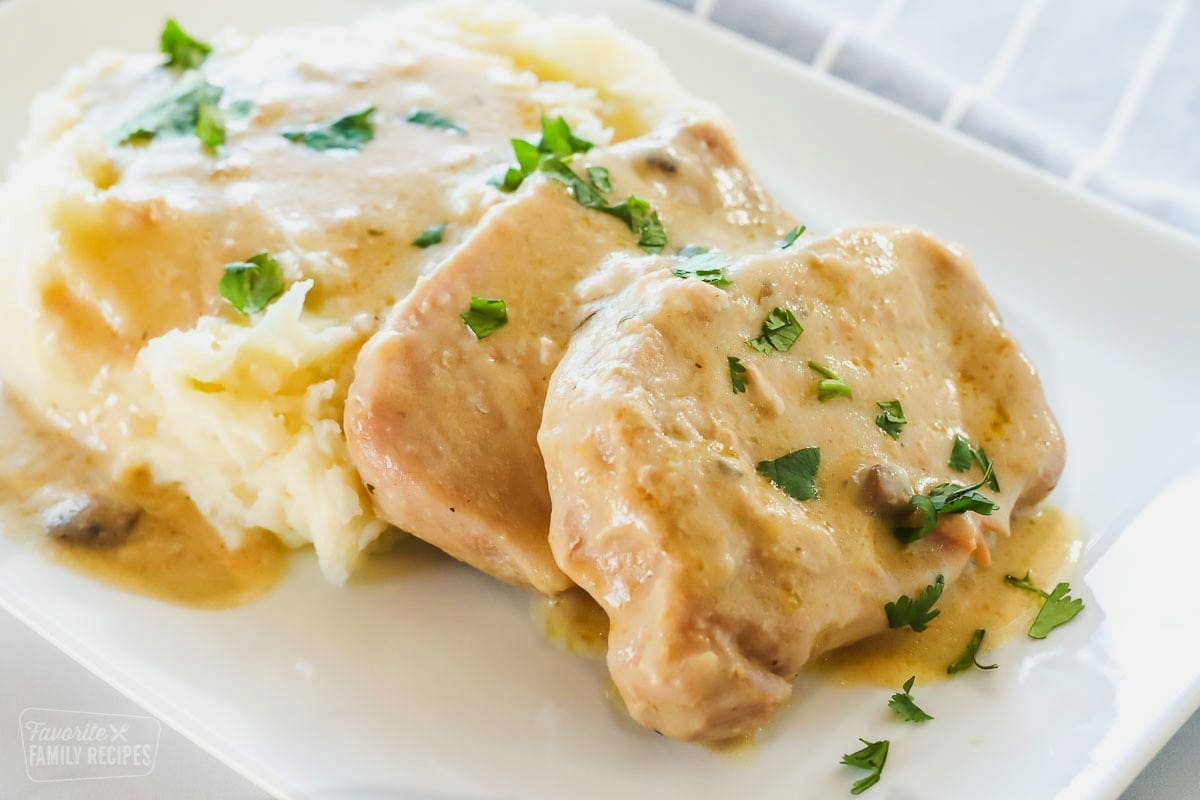 Two pork chops on a white plate with mashed potatoes and gravy on the side