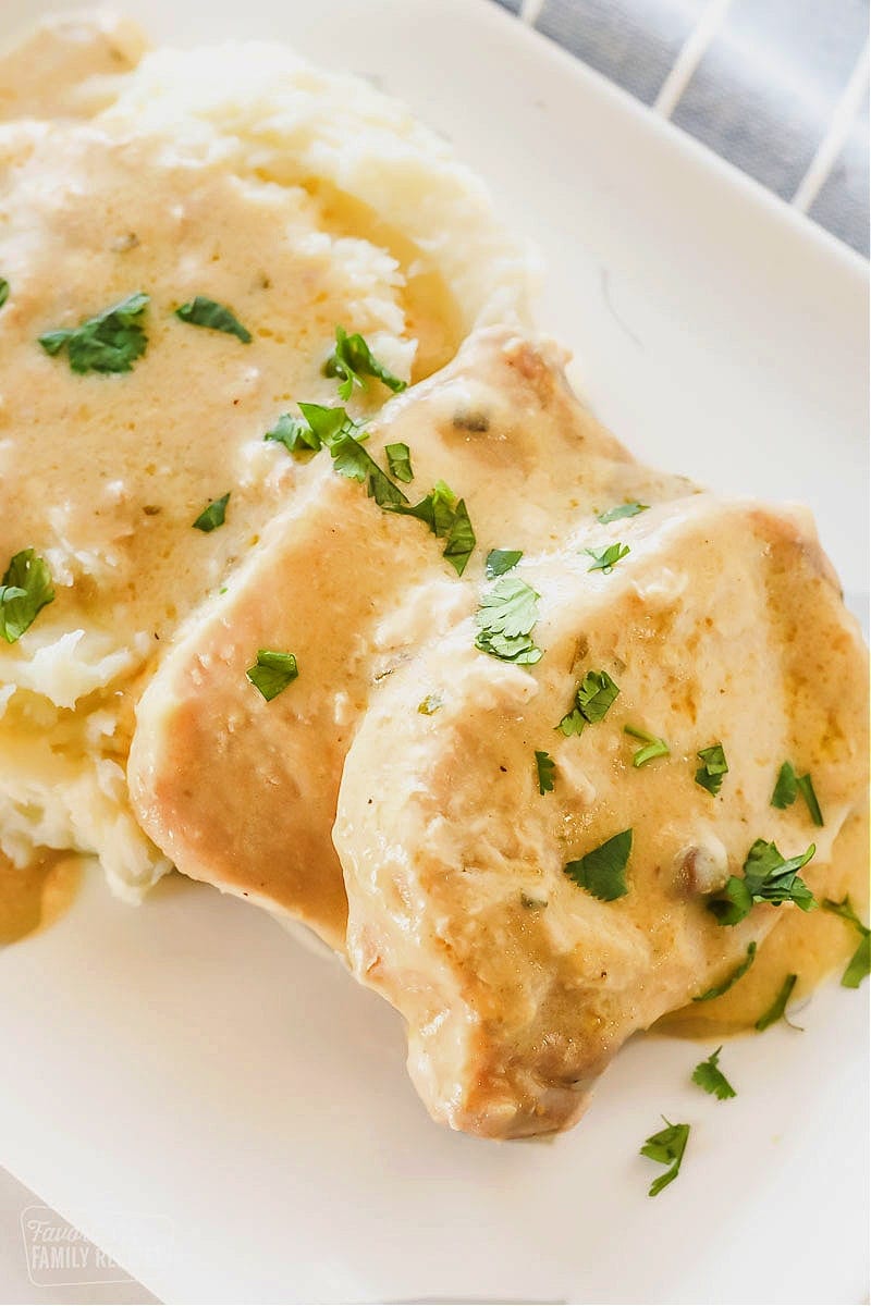 A tray of crock pot pork chops with gravy sprinkled with parsley