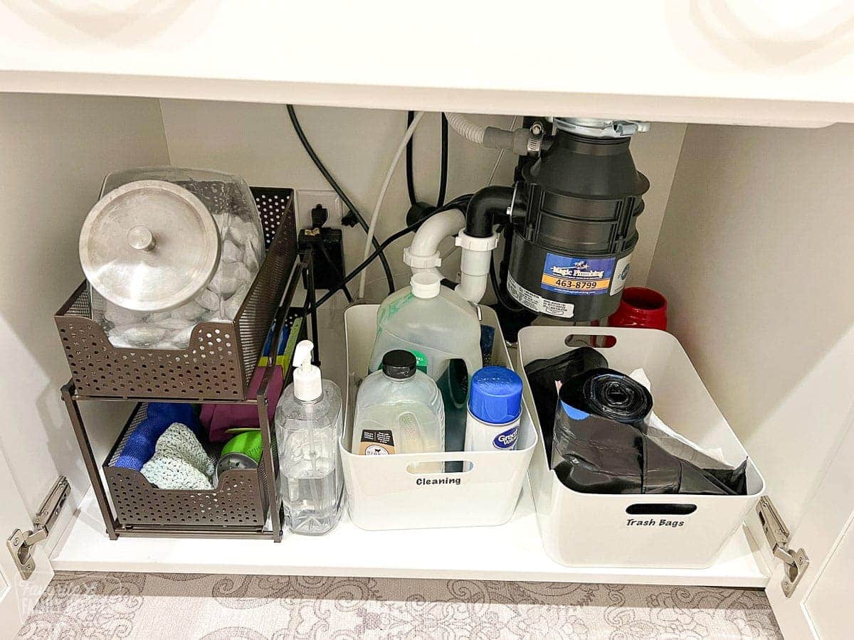 Cleaning supplies and trash bags organized under a sink