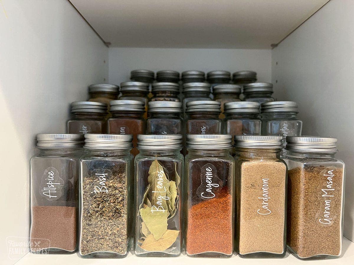 Spices and herbs neatly organized in a cupboard on risers