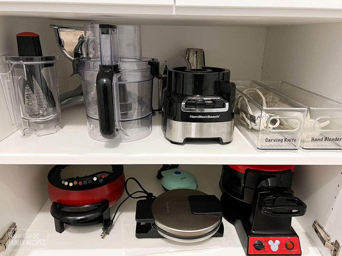 Small appliances in a kitchen cupboard that have been organized neatly