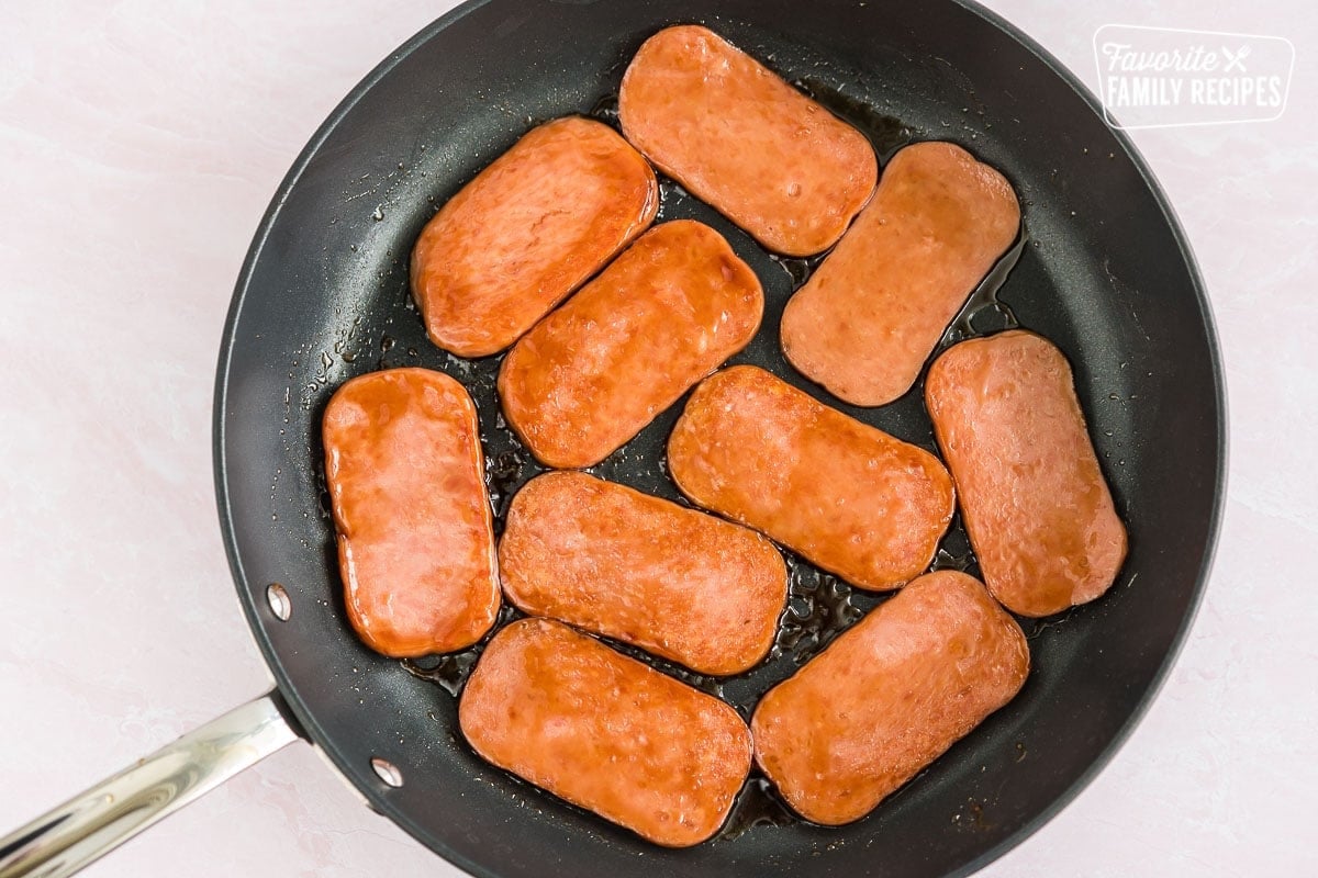 Sliced Spam frying in a skillet, preparing the meat for Hawaiian Spam Musubi recipe.