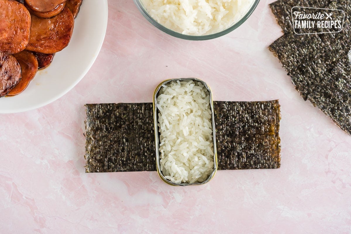A spam musubi mold filled with sushi rice with a plate of spam on the side.