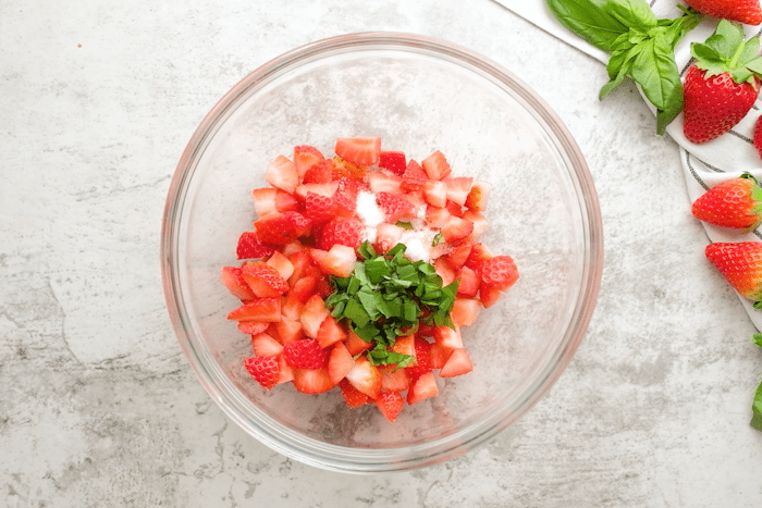 Strawberries, sugar, and basil combined in a bowl for Strawberry Bruschetta.