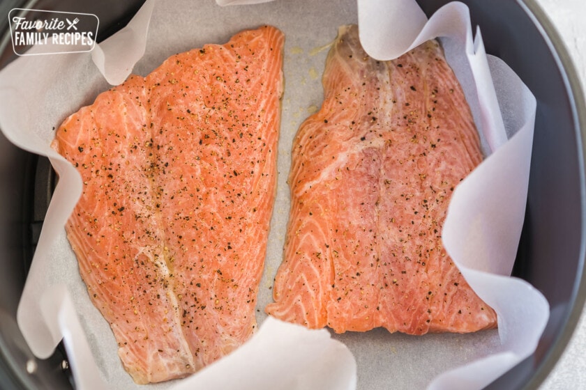 Two seasoned salmon filets on a piece of parchment paper in an air fryer basket