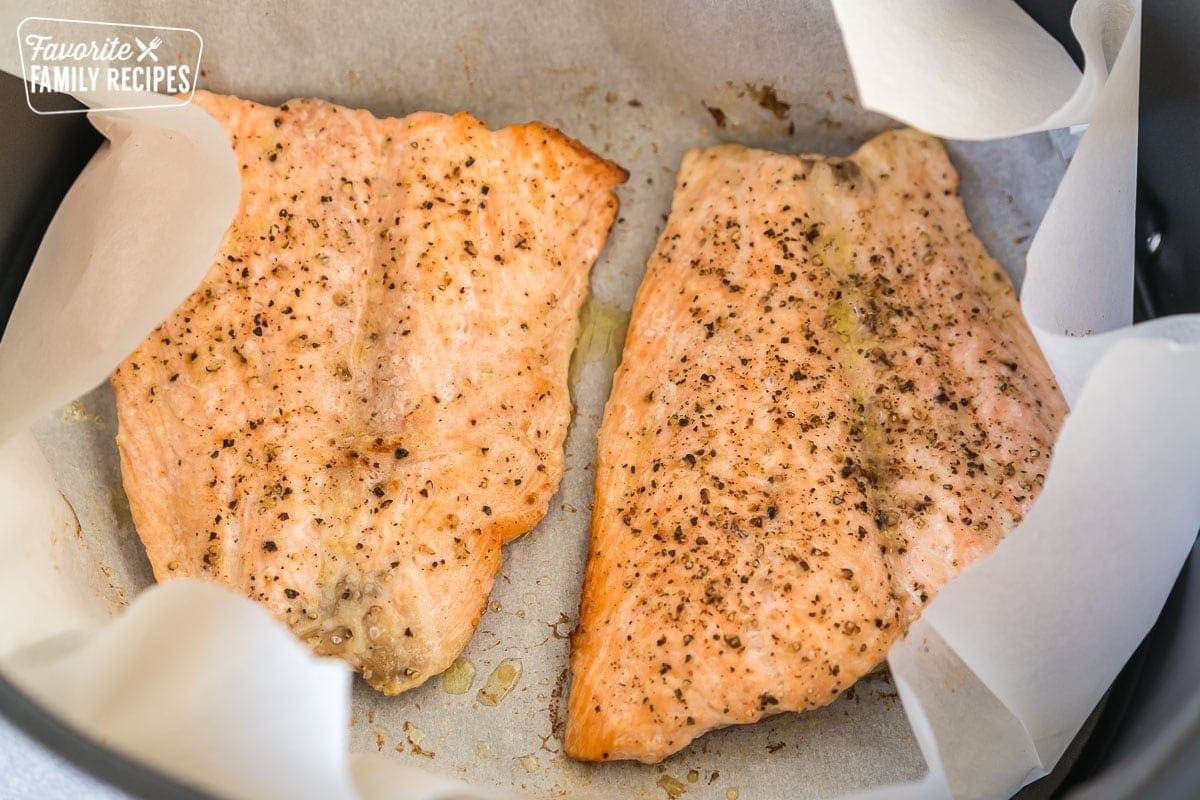 Two cooked salmon filets in an air fryer basket