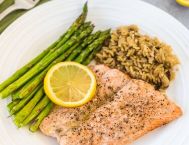 A large plate with asparagus, wild rice, and air fryer salmon topped with a lemon slice