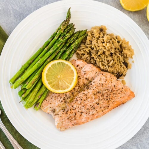 A large plate with asparagus, wild rice, and air fryer salmon topped with a lemon slice