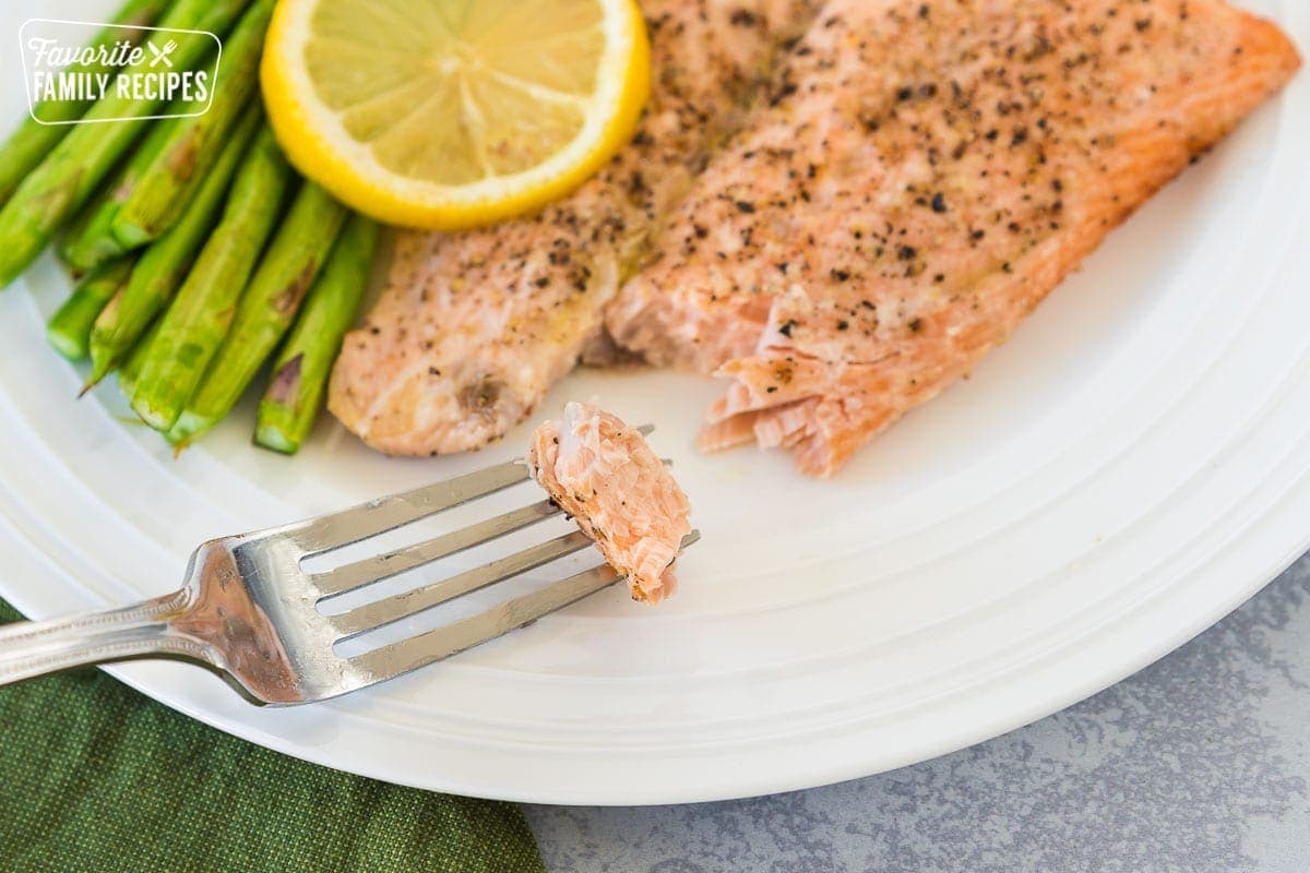 A fork taking a bite of salmon from a plate