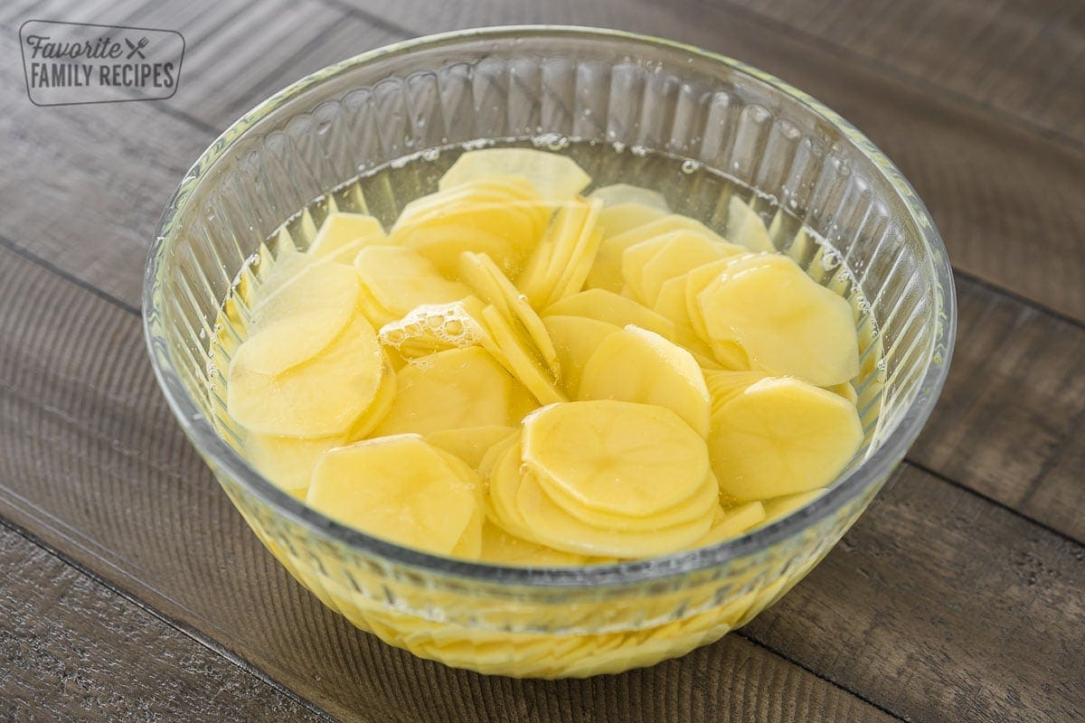 Thinly sliced and peeled potatoes in a large bowl of water