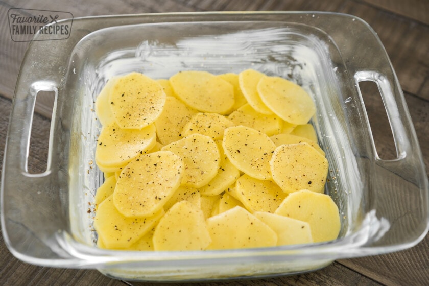 A layer of thinly sliced potatoes in the bottom of a baking dish topped with salt and pepper