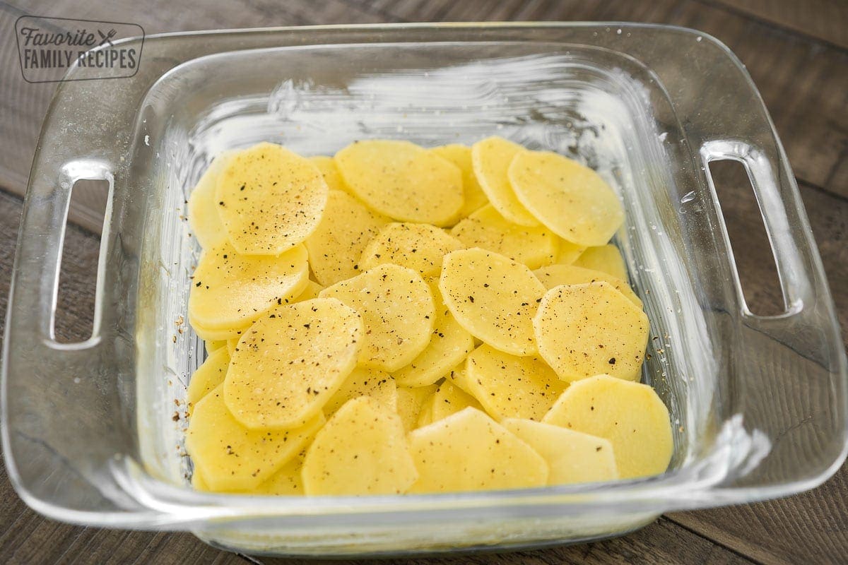 A layer of thinly sliced potatoes in the bottom of a baking dish topped with salt and pepper