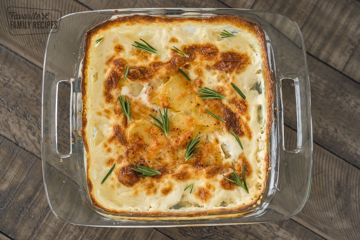 Au Gratin Potatoes baked in a square glass baking dish topped with rosemary